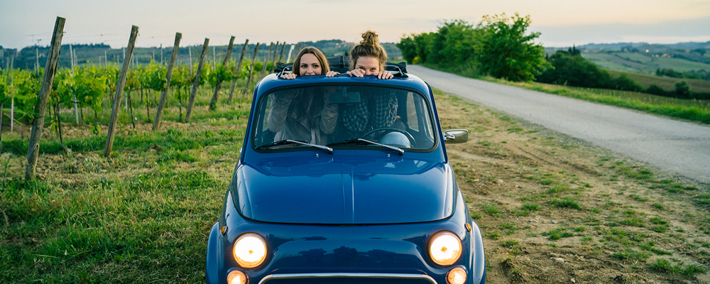 Two women sitting in small car next to a vineyard